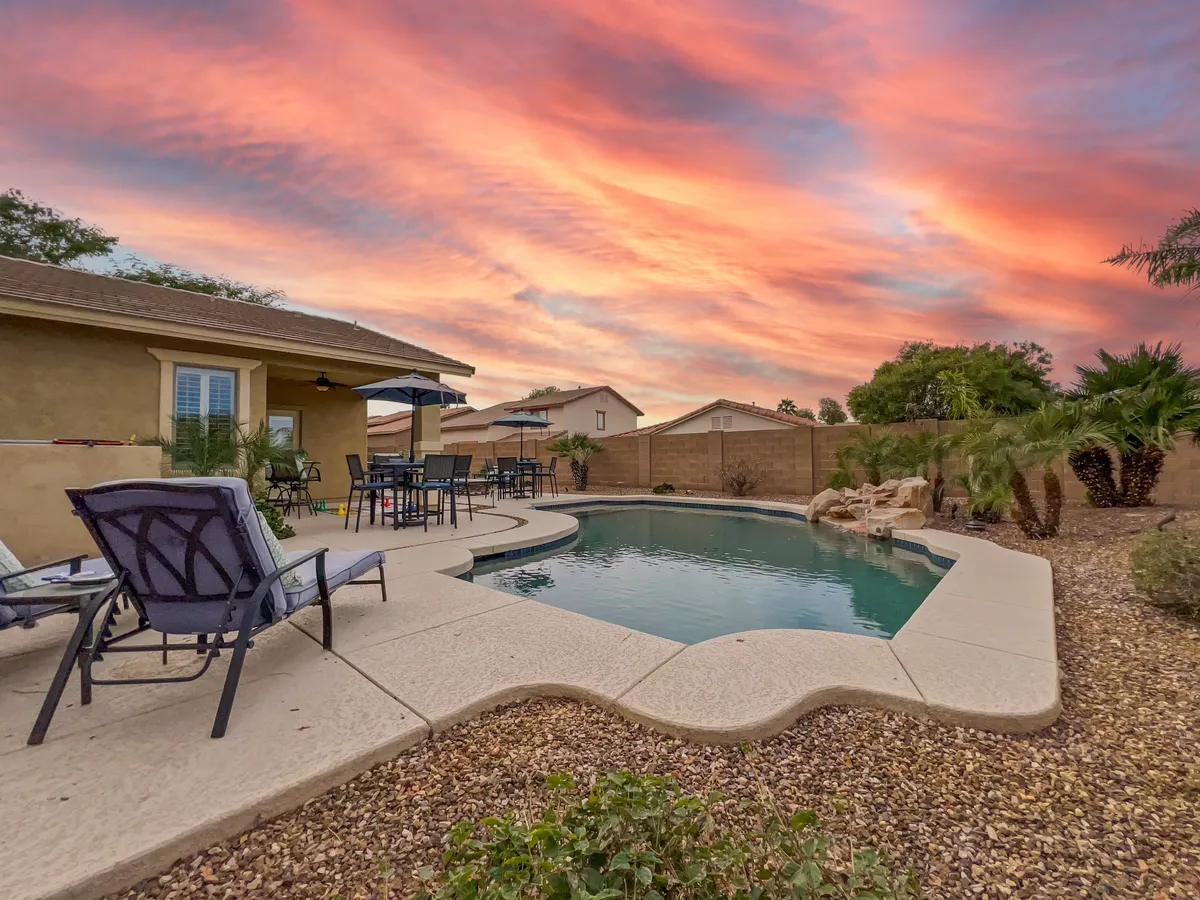 This image shows a private backyard oasis with a sparkling swimming pool and comfortable patio furniture surrounded by lush landscaping. The setting is serene and inviting, perfect for relaxing or unwinding after a productive workday. The space captures the essence of outdoor leisure and comfort.