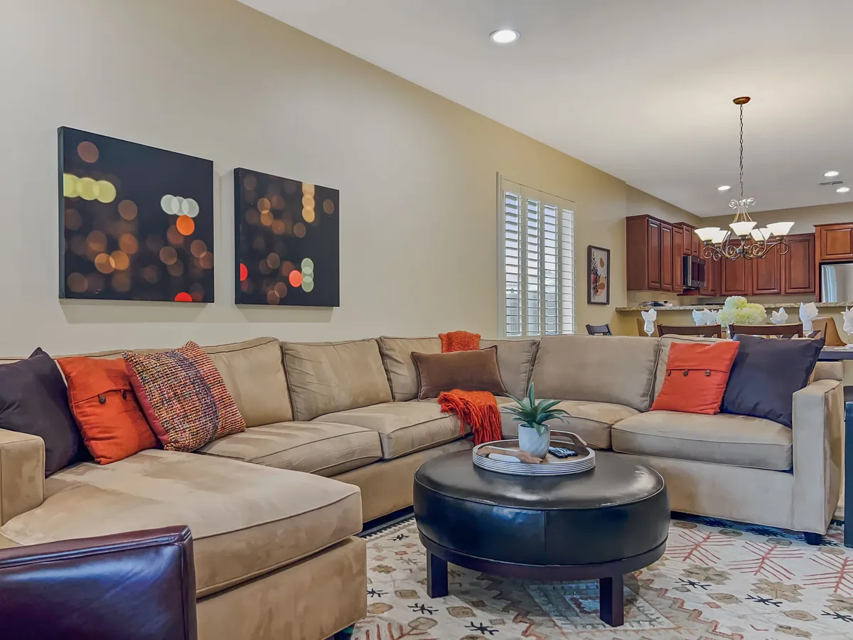 A large, comfortable sectional sofa with colorful throw pillows anchors a living space that feels both cozy and inviting. A coffee table with a plant and abstract wall art add character, while ample natural light brightens the room, suggesting a seamless transition from outdoor to indoor relaxation after a day of adventure.