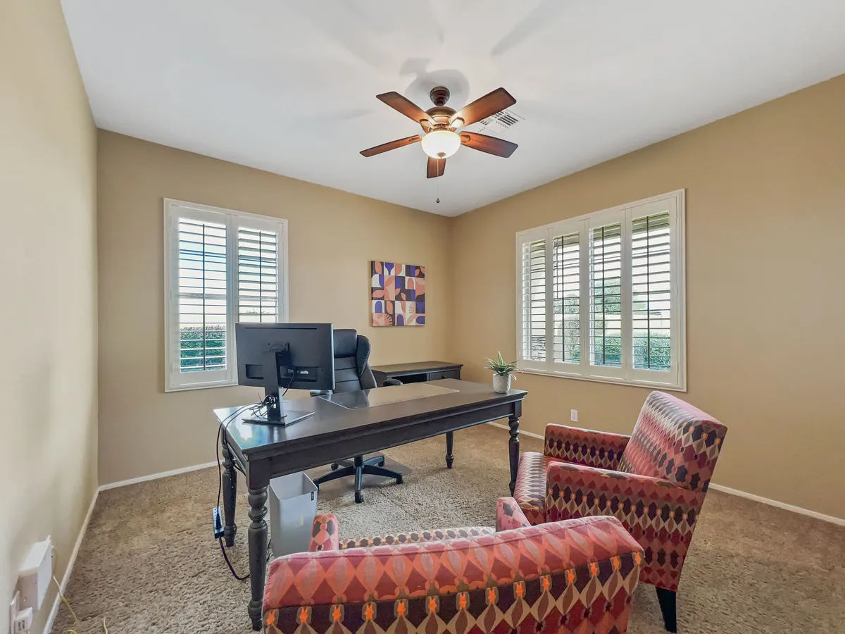 This interior scene centers around a modern desk setup with a computer, chairs, and vibrant artwork on the walls. Ample windows bring in natural light, creating an inviting and productive atmosphere ideal for working, reading, or video calls.