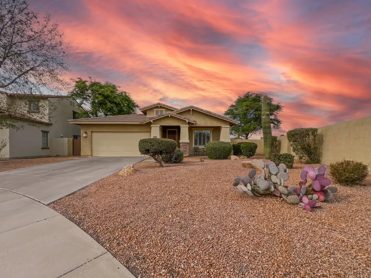 A wide view of the home's exterior set against a colorful sky, with cacti and desert landscaping in the foreground. The inviting porch hints at relaxed outdoor living and gatherings, while the overall composition situates the property within its vibrant community.