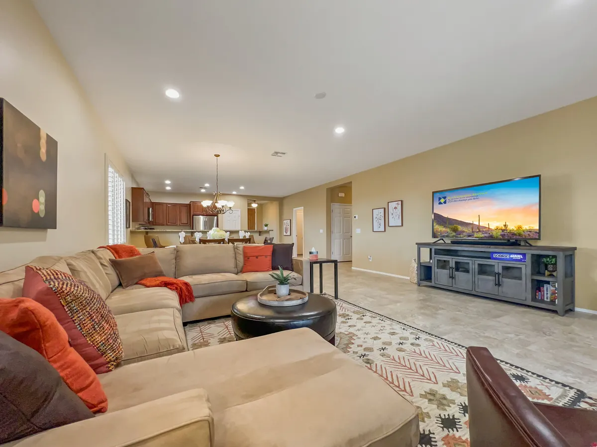 A spacious great room featuring a large sectional sofa, a coffee table, and a wall-mounted TV, all arranged for optimal relaxation and socializing. Decorative artwork and abundant natural light enhance the inviting ambiance, making this an ideal space for movie nights or gathering with friends and family.