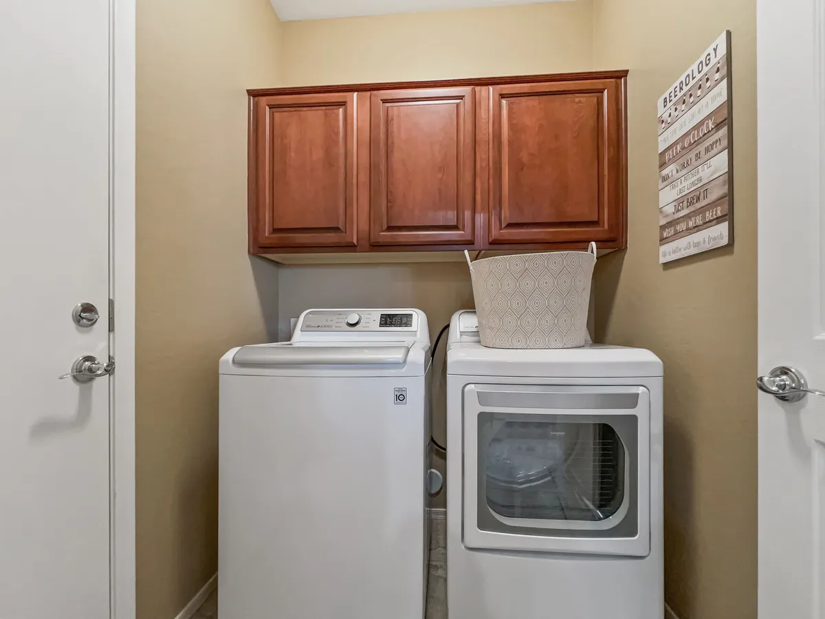 A well-appointed laundry room featuring a washing machine, dryer, wooden cabinetry, and a decorative wall sign. The space is organized and practical, providing convenience for daily routines and longer stays.