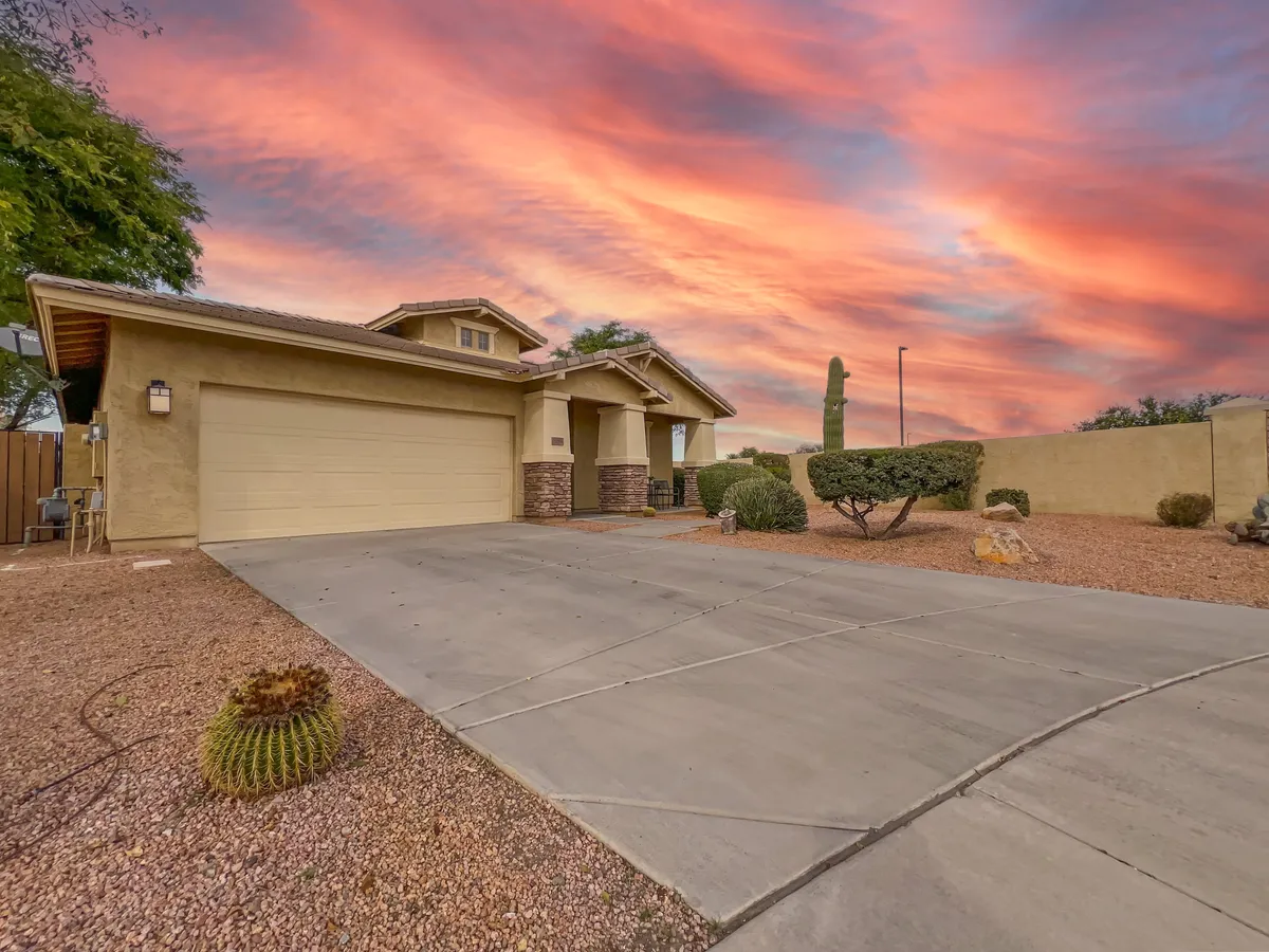 The front facade of a home is framed by a landscaped yard and a dramatically colorful sunset sky. The scene evokes a welcoming, serene neighborhood setting, perfect for relaxing on the porch or gathering with neighbors.
