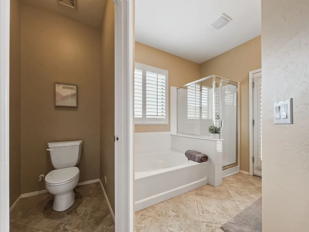 A tranquil bathroom featuring a deep bathtub, glass shower enclosure, toilet, towel, and framed artwork. The space is serene and inviting, perfect for relaxing soaks or refreshing morning showers.