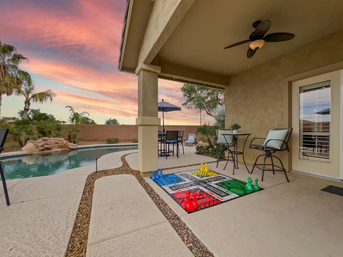 This image features an inviting backyard scene with a sparkling swimming pool, a game mat on the pool deck, an outdoor seating area, and a sky tinged with sunset colors. The mood is playful and relaxed, ideal for outdoor family gatherings and fun.