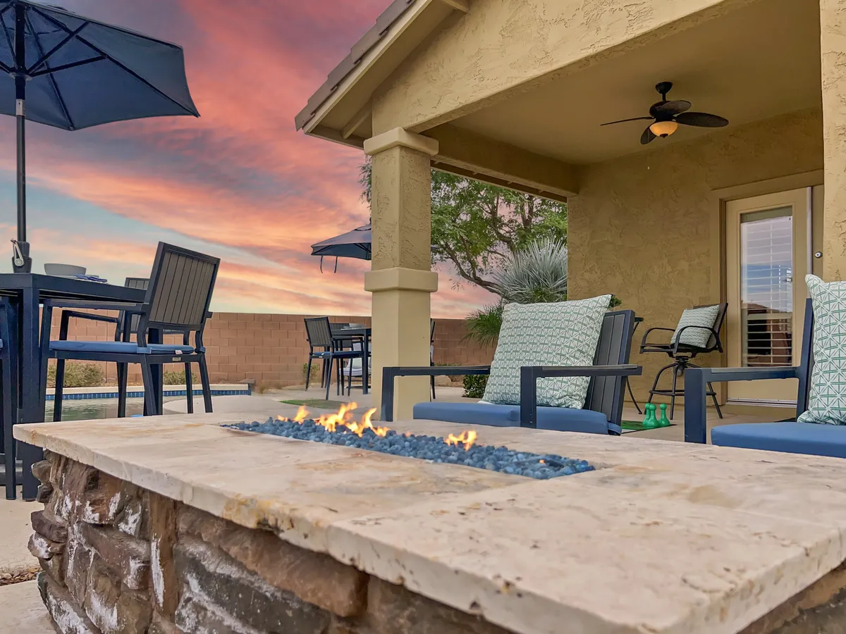 A cozy outdoor space showcasing a fire pit surrounded by lounge chairs and a dining table, set against a beautiful sunset sky. The atmosphere is tranquil and inviting, ideal for relaxing or socializing outdoors.