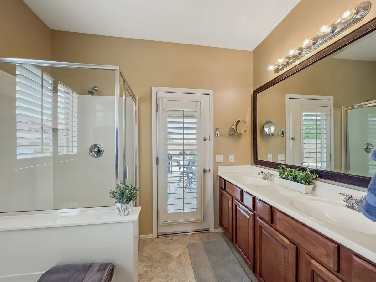A modern bathroom with a double vanity, glass shower enclosure, decorative plants, and a large mirror. The space feels calm, organized, and spa-like—ideal for rejuvenating routines.