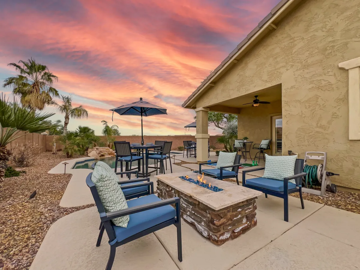 A welcoming exterior setting featuring a fire pit surrounded by outdoor seating and umbrellas, with the sky awash in sunset colors. The arrangement encourages social gatherings and cozy evenings, perfect for relaxing by the fire and enjoying Arizona nights.