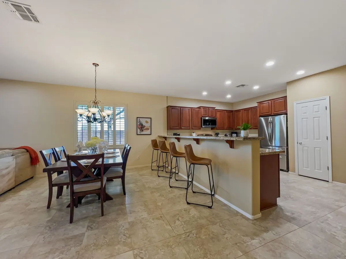An open-concept living space with a seamless transition between the dining area, kitchen bar with stools, and a comfortable sofa. The kitchen cabinets and dining table are easily accessible from the living area, highlighting the home's connected layout and suitability for casual gatherings or festive meals.